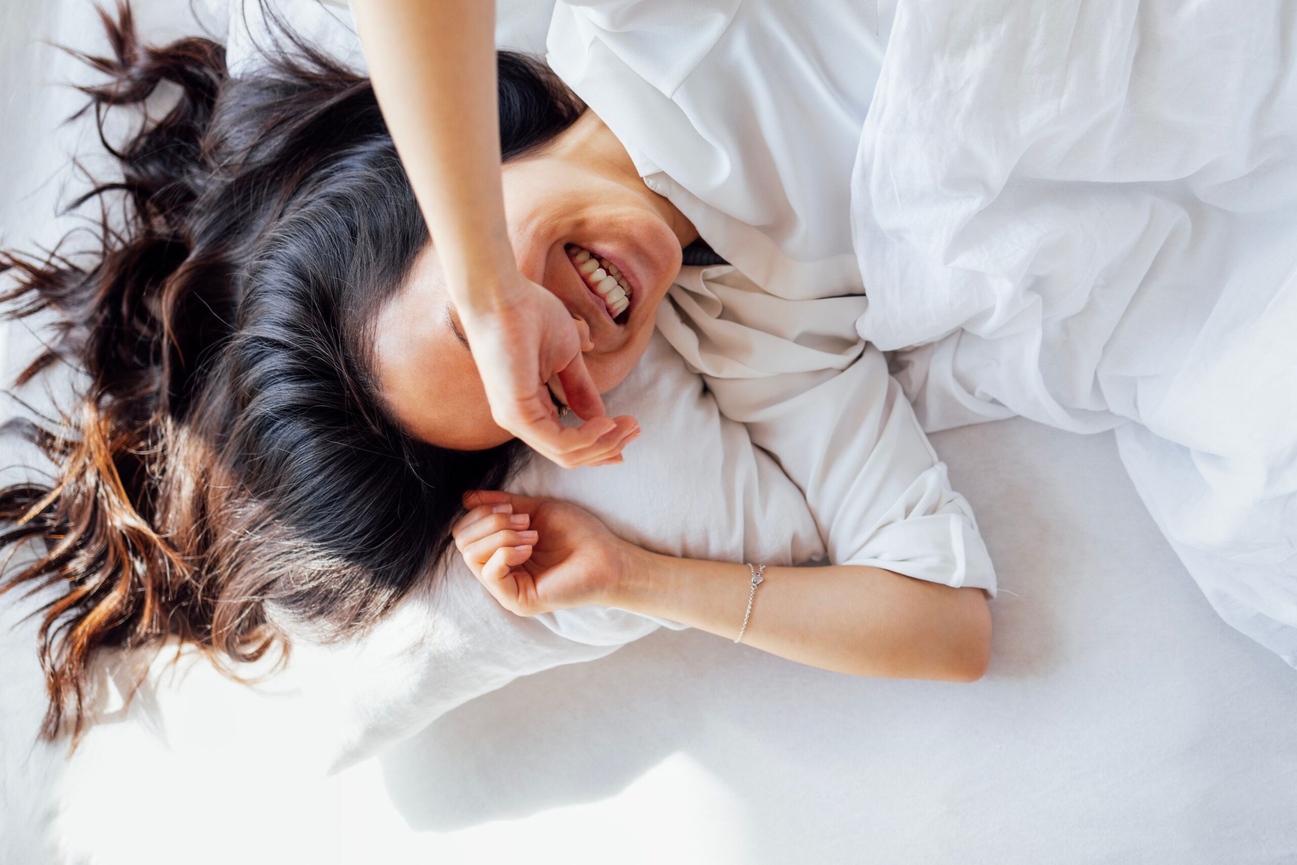 smiling woman in white shirt laying in bright white bed