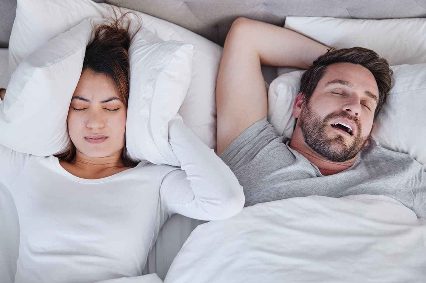 man snoring woman covering ears with pillow